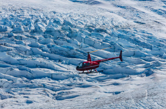 Red helicopter flying above an Alaska glacier on a glacier safari