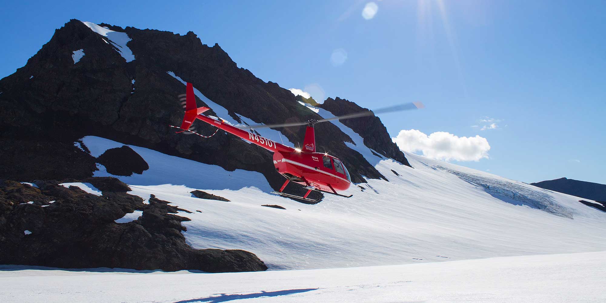 Red helicopter flying above an Alaska snowfield