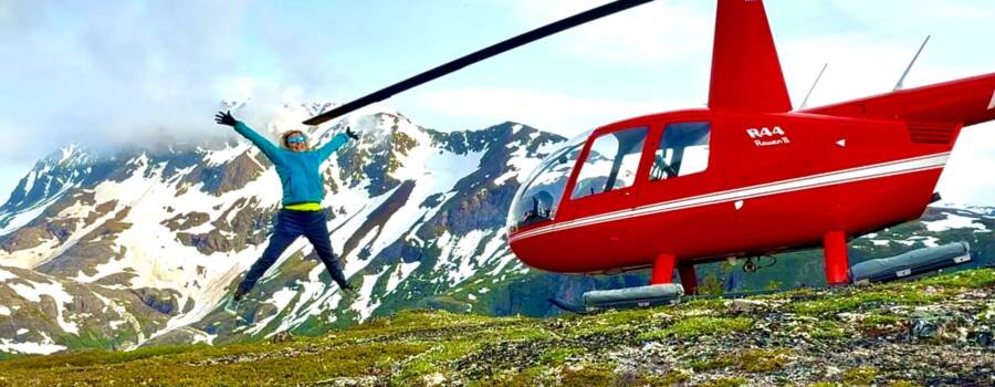 Red helicopter landing in remote Alaska mountains for a helicopter bear viewing tour